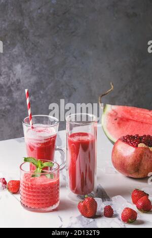 Three different red fruit berry watermelon, strawberry, raspberry, pomegranate cocktails or smoothies in glasses with crushed ice, fresh mint and ingr Stock Photo