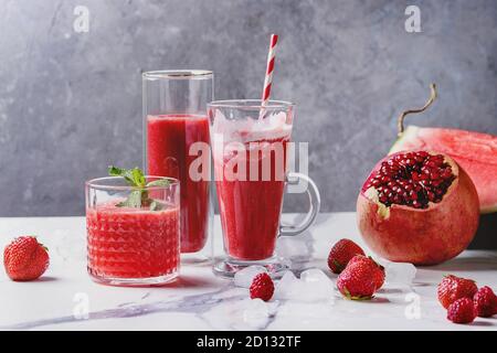 Three different red fruit berry watermelon, strawberry, raspberry, pomegranate cocktails or smoothies in glasses with crushed ice, fresh mint and ingr Stock Photo