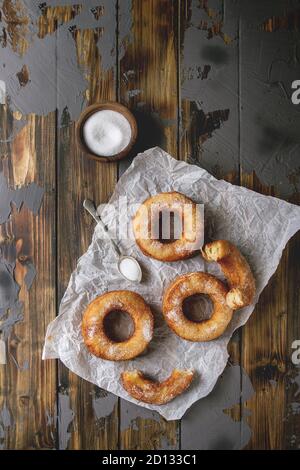 Homemade puff pastry deep fried donuts or cronuts in stack with sugar standing on crumpled paper over dark wooden concrete texture background. Flat la Stock Photo