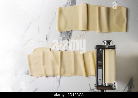 Rolled dough for homemade italian uncooked pasta lasagna from pasta machine maker with semolina flour over white marble texture background. Flat lay, Stock Photo