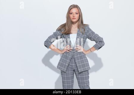 Tough fashion businesswoman holding hands on hips and wearing suit while standing on white studio background Stock Photo