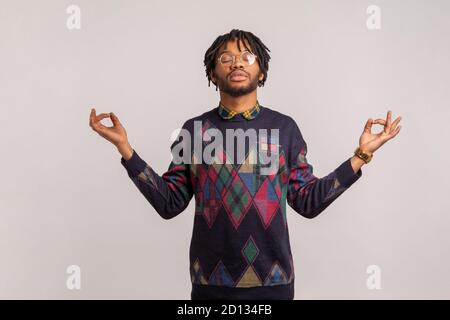 Peaceful calm african man with dreadlocks in glasses standing with closed eyes and mudra gesture, meditating trying to concentrate, inspiration. Indoo Stock Photo