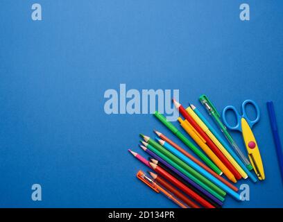 plastic scissors and multicolored wooden pencils on a blue background, flat lay, copy space Stock Photo