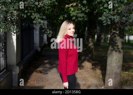 young blonde woman in warm sweater outdoors. woman smiles and rejoices in the autumn sun. last sunny days of autumn Stock Photo