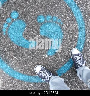 Man standing on blue dot. Sign painted on the pavement reminding users to maintain a physical distance of 3 feet / 1 meter during the COVID-19 pandemi Stock Photo