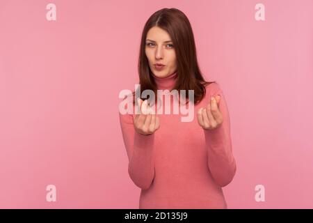 Greedy mercantile woman with brown hair in pink sweater asking cash showing money gesture with fingers seriously looking at camera. Indoor studio shot Stock Photo