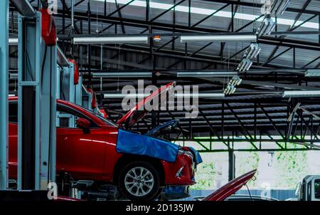 Auto repair shop. Red SUV car is lift in garage for repair and maintenance service. Auto service with lifted vehicle. Car body lifted in workshop. Stock Photo