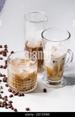 Iced coffee cocktail or frappe with ice cubes and cream served in three different glasses with coffee beans around on white marble table. Stock Photo