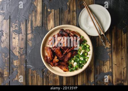 Chinese traditional dish Cantonese BBQ Pork Belly with spring onion served in ceramic plate with chopsticks over dark wooden plank background. Flat la Stock Photo