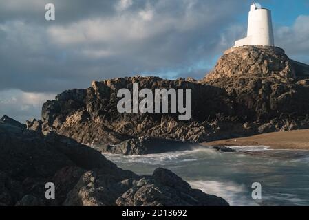 Spray topped waves roll into the beach below the lighthouse at Llanddwyn, Anglesey, Wales Stock Photo