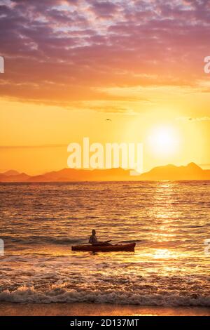 A canoeist at dawn with the sun rising over a calm, tropical ocean bay and distant hills Stock Photo