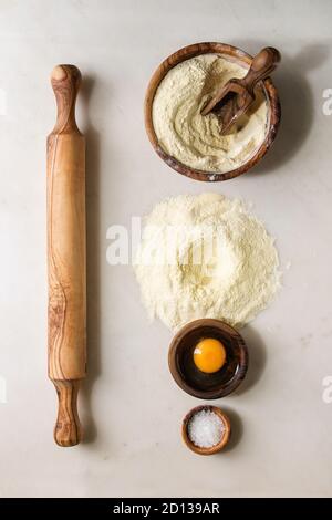 Ingredients for homemade italian pasta ravioli cooking semolina flour, egg yolk, sea salt with olive wood utensils bowls, scoop and rolling pin over w Stock Photo