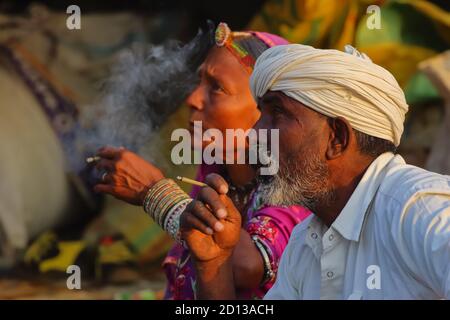 Selective focus image of a tribal man and women siting and smoking local Indian cigar together at Pushkar, Rajasthan, India on 29 October 2017 Stock Photo