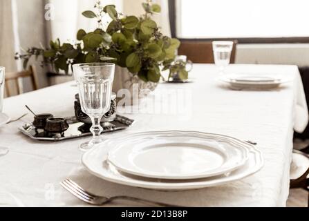 Decorated boho table. The table is covered with a tablecloth, plates, glasses and a vase with a green plant Stock Photo