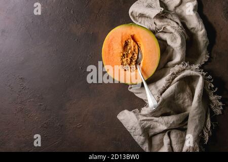 Half of ripe organic Cantaloupe melon with seeds and spoon inside on cloth textile over dark brown texture background. Flat lay, space Stock Photo