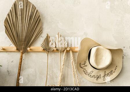 Fan leaf and straw hat hang on wooden hanger against gray wall Stock Photo