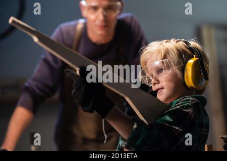 an experienced carpenter teacher taught a lesson for a small boy, who made a wooden gun and shows it to the master Stock Photo