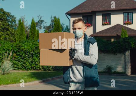 Delivery man with two boxes stands outside the house and looks at the camera Stock Photo