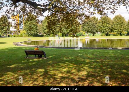 Boating lake pond in Victoria Park, Newbury, Berkshire, England, UK person sitting on bench alone Stock Photo