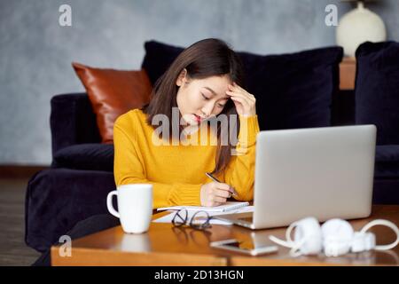 Asian woman working at home, writing notebook, freelancer. Overworking, filling out papers Stock Photo