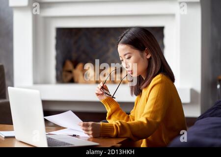 Asian woman working at home looking at documents. Beautiful Japanese female Stock Photo
