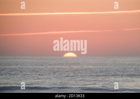 Big sun setting on the ocean, almost disappearing the horizon line, with warm and strong orange tone Stock Photo