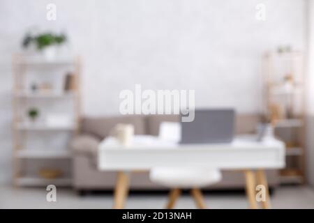 Home office, workspace for remote work. Sofa, chair and table with laptop and cup in interior of living room during COVID-19 pandemic Stock Photo
