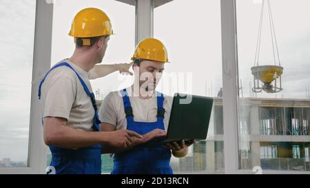 Two builders wearing protective helmets working on a laptop. Stock Photo