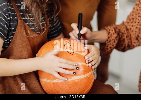 young girl sitting at a table, decorating pumpkins. Halloween holiday and family lifestyle background. little girl paints a pumpkin for Halloween Stock Photo