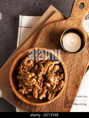 A handful of peeled walnuts on a wooden plate on a background of wooden boards and candles. Stock Photo