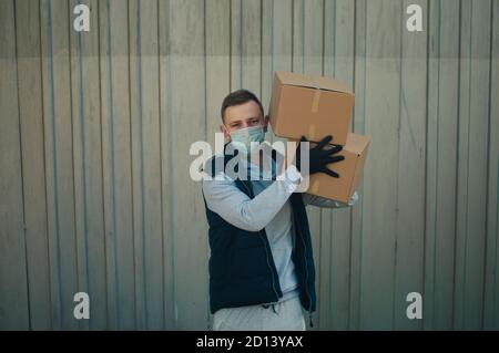 Covid delivery man holds two boxes on shoulder stands against a gray background Stock Photo