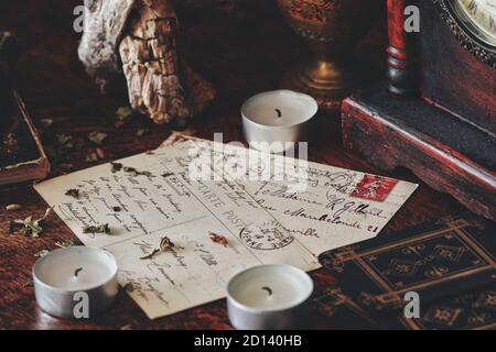 Close up of hand written letters to loved ones. Old vintage worn postcards with black ink writings in cursive. White candles, herbs, tree bark, tarot Stock Photo