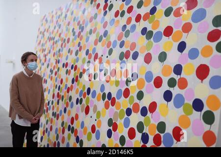 A gallery staff member poses next to 'Spot Painting', 1986, during a preview of Damien Hirst's solo exhibition titled 'End of a Century' at Newport Street Gallery in London, which will feature over fifty artworks spanning Hirst's formative years as a student in the 1980s to becoming one of Britain's leading contemporary artists during the 1990s. Stock Photo