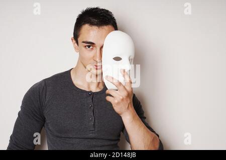 young man taking off white mask revealing face and identity - with copy space Stock Photo