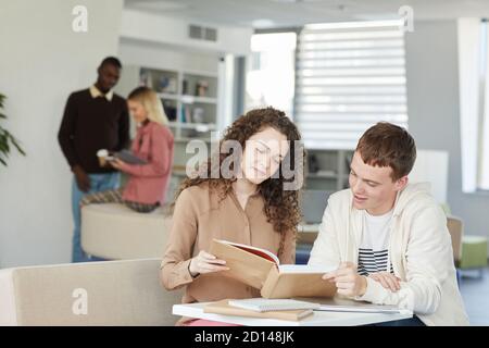 Portrait of two young students boy ad girl studying together while sitting at table in college library and smiling, copy space Stock Photo