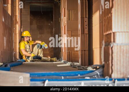 Construction Industry Caucasian Builder Worker Resting on the Floor Between Raw Newly Constructed Ceramic Wall Bricks Stock Photo