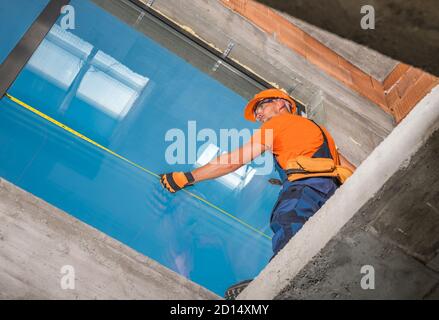 Caucasian Windows Technician Finishing Commercial Building Large Format Aluminium Window Installation. Final Measuring. Construction Industry Theme. Stock Photo