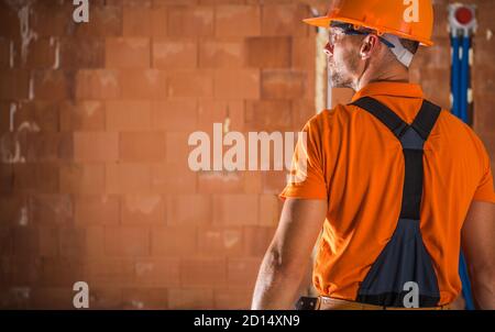 Caucasian Construction Industry Worker in His 40s Wearing Orange Hard Hat and Safety Glasses Preparing For Another Full Day on the Construction Site. Stock Photo