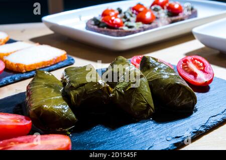 Dolma, delicious Casucasian and Turkish cuisine, vine leaves stuffed with minced meat and rice. Italian bruschetta with tomatoes and cheese in backgro Stock Photo