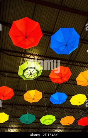 Brightly coloured umbrellas hanging from metal ceiling of industrial style building Stock Photo
