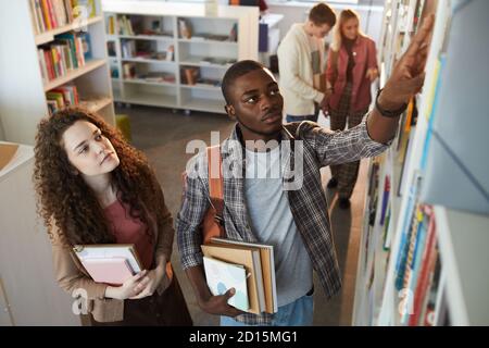High angle portrait of two students taking books off shelf in school library, copy space Stock Photo