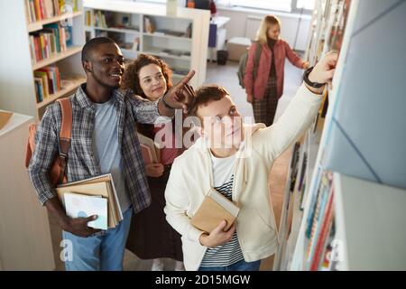 High angle view at multi-ethnic group of students taking books off shelf in school library, copy space Stock Photo