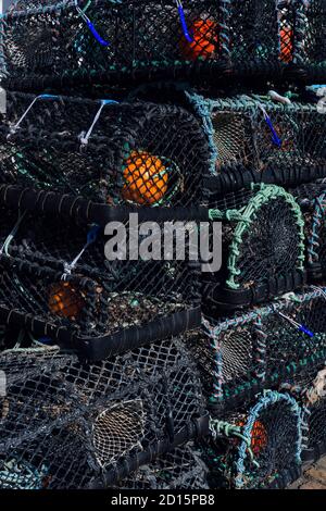 Crab and lobster pots or creels stacked ready for use by the small fleet of boats based in the picturesque harbour at Mullion Cove on the Lizard Peninsula in Cornwall, England, UK.  Mullion Cove, on the Lizard Heritage Coast, is owned and managed by the National Trust, which also owns Lizard Point, the most southerly place in mainland Britain. Stock Photo