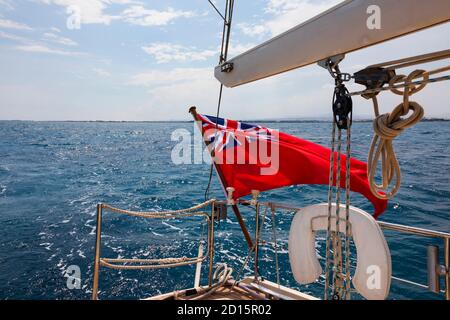 British Red Ensign flag flying on the stern of a yacht under sail in the Mediterranean Sea, off the coast of Cyprus. Cyprus Stock Photo