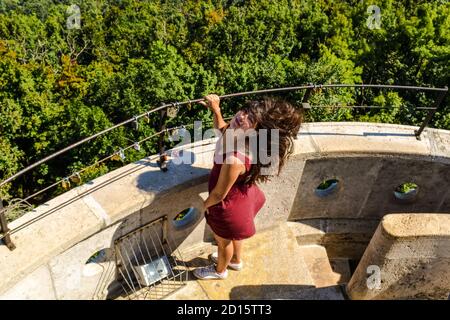 beautiful young girl with black hair fluttering in the wind stands on historic tower Elizabeth Lookout on Janos Hill in Budapest, Hungary Stock Photo