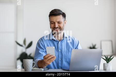 Handsome male office manager using smartphone at workplace, sitting at desk Stock Photo