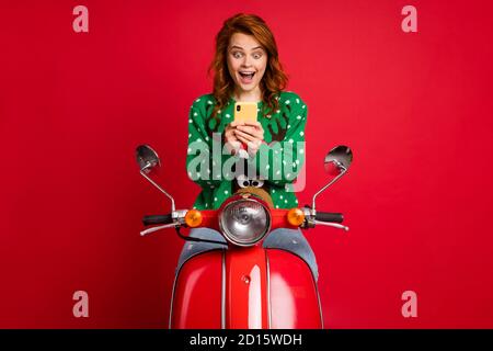 Photo portrait of screaming red-haired biker rider holding phone in two hands wearing ugly green jumper sweater isolated on vivid red colored Stock Photo