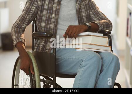 Cropped portrait of unrecognizable African-American man using wheelchair in school in library with focus on books, copy space Stock Photo