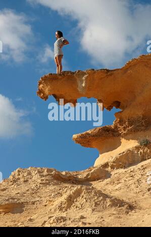 Spain, Balearic islands, formentera, calo des mort, woman in a striped tee shirt advanced on a red rock formation in front of the sea Stock Photo