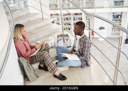 High angle portrait of two students chatting while sitting on stairs in college and working on homework, copy space Stock Photo